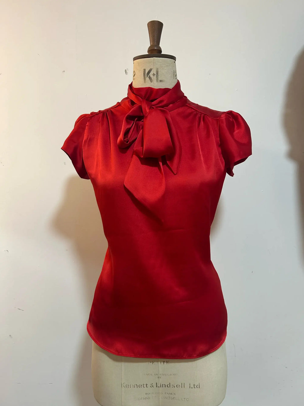 A red blouse with cap sleeves and a silky tie neck displayed on a mannequin.