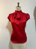 A red blouse with cap sleeves and a silky tie neck displayed on a mannequin.