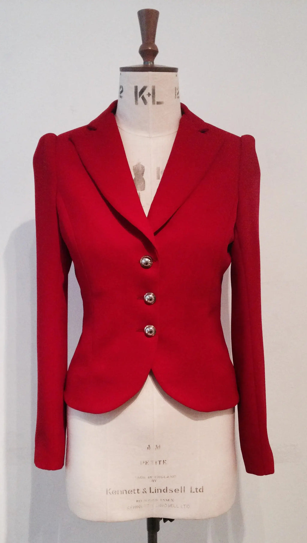 A red jacket with a 3-button closure and triple frill detail at the back displayed on a mannequin.