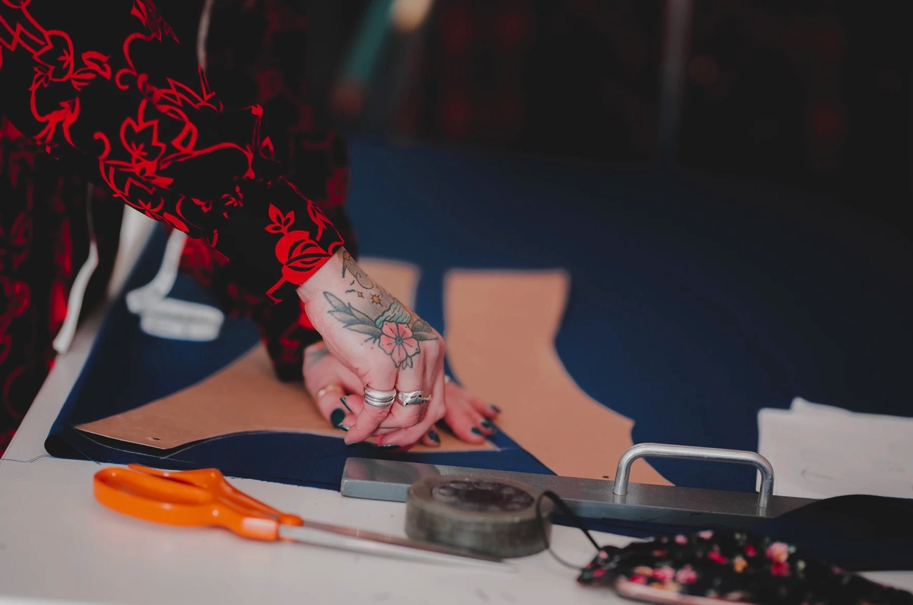 Person with tattoos holding a knife on a table with scissors and tape.