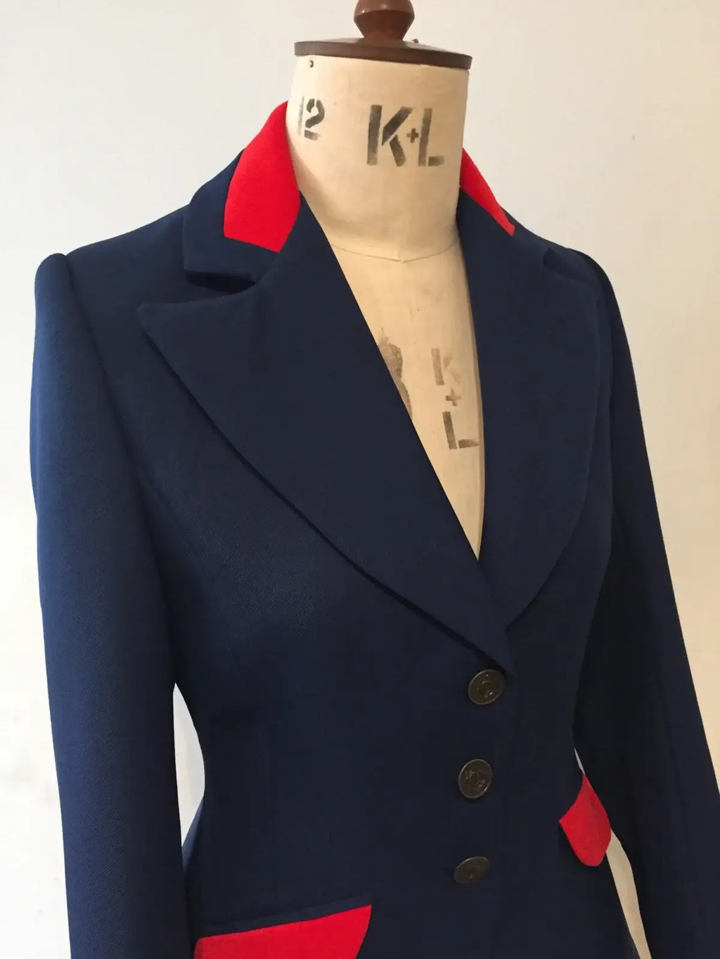 A navy long-line swing jacket with red velvet detailing on the collar and trim, displayed on a mannequin.