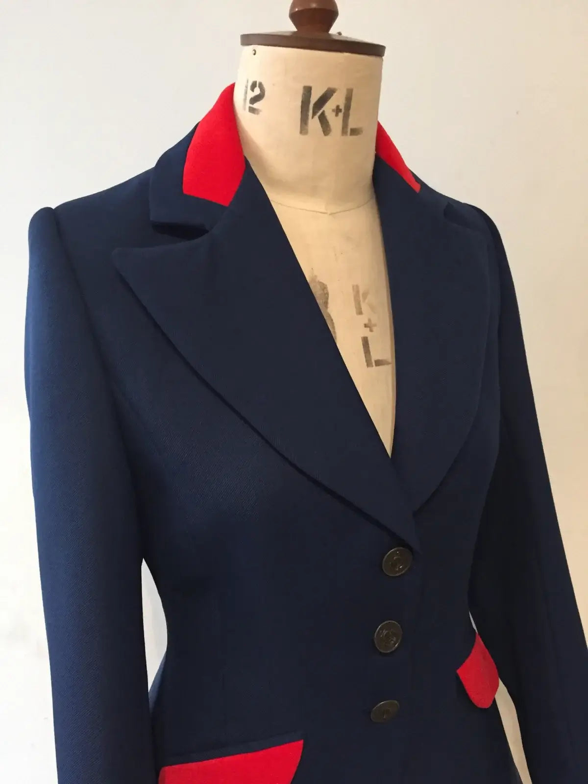 A navy long-line swing jacket with red velvet detailing on the collar and trim, displayed on a mannequin.