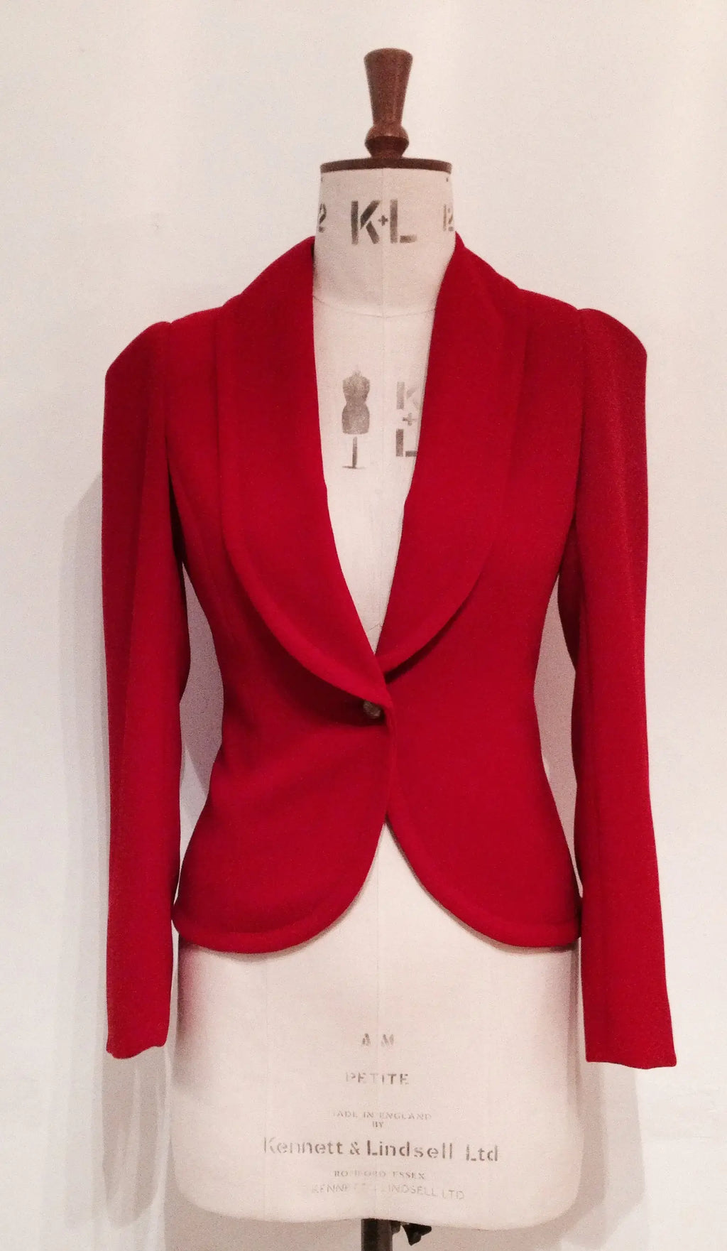 A red show jacket displayed on a mannequin, featuring a shawl collar, single-button closure, and a half-belt design.