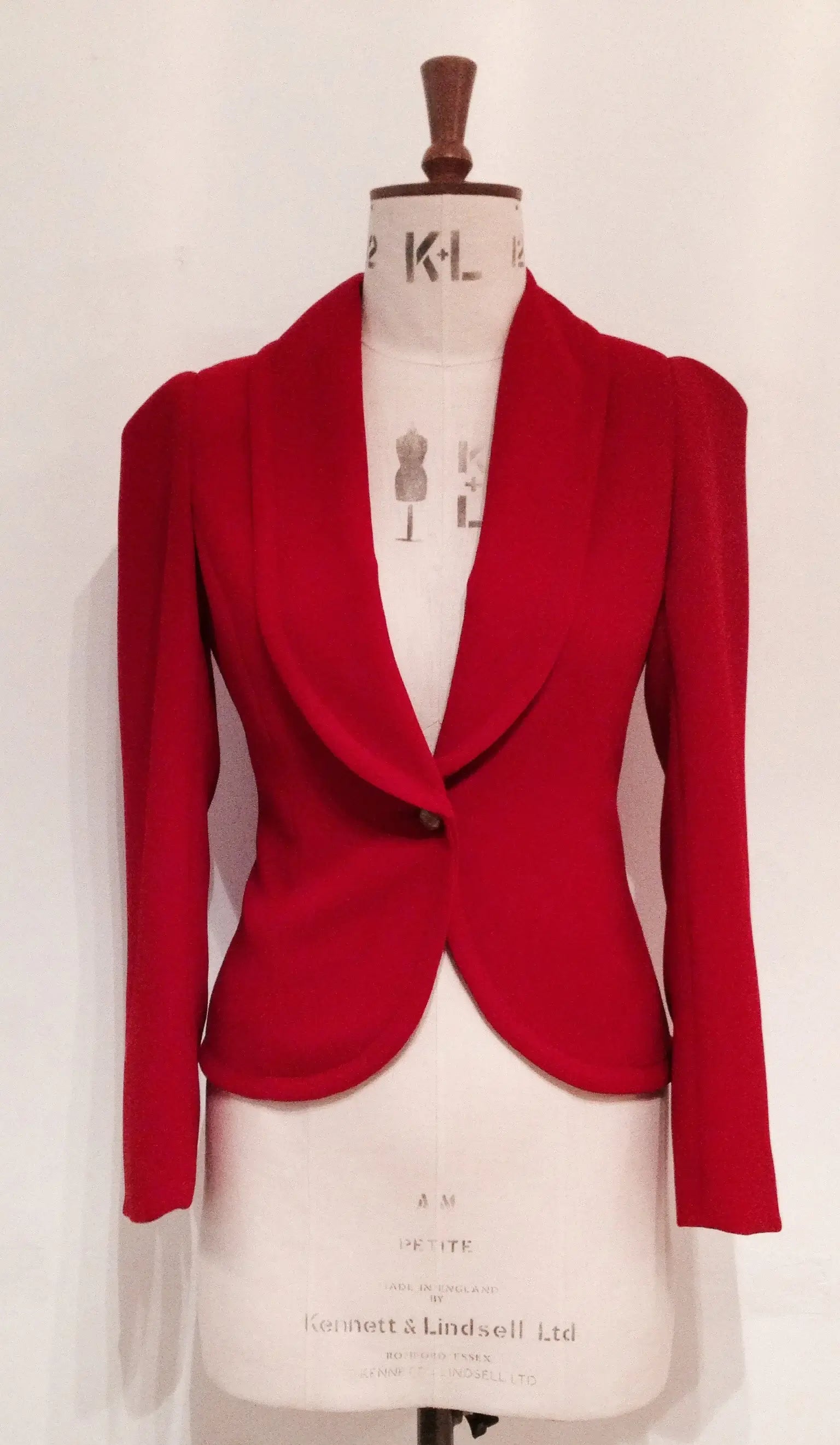 A red show jacket displayed on a mannequin, featuring a shawl collar, single-button closure, and a half-belt design.