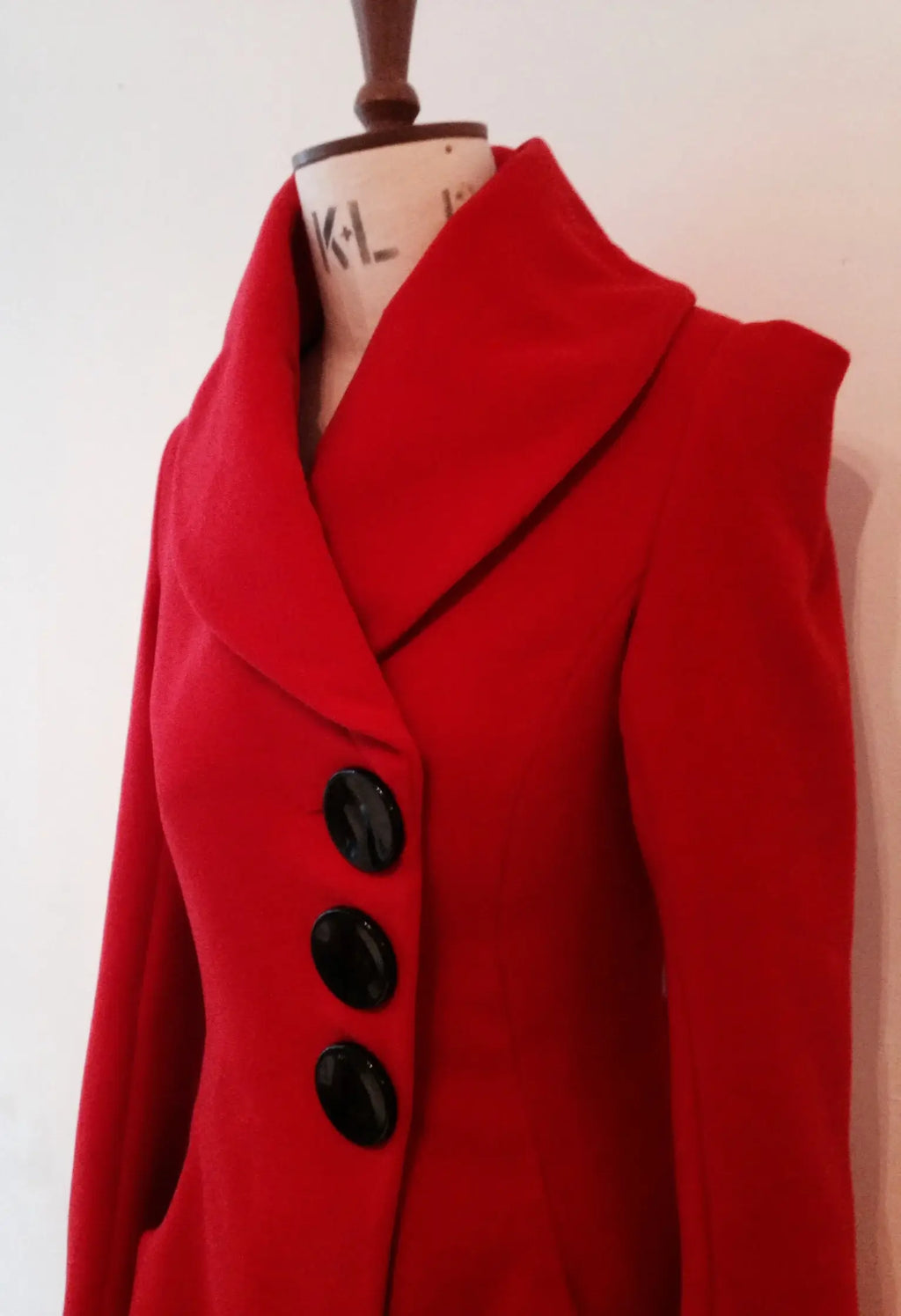 A red swing coat with a shawl collar and three large buttons, displayed on a mannequin against a plain background.