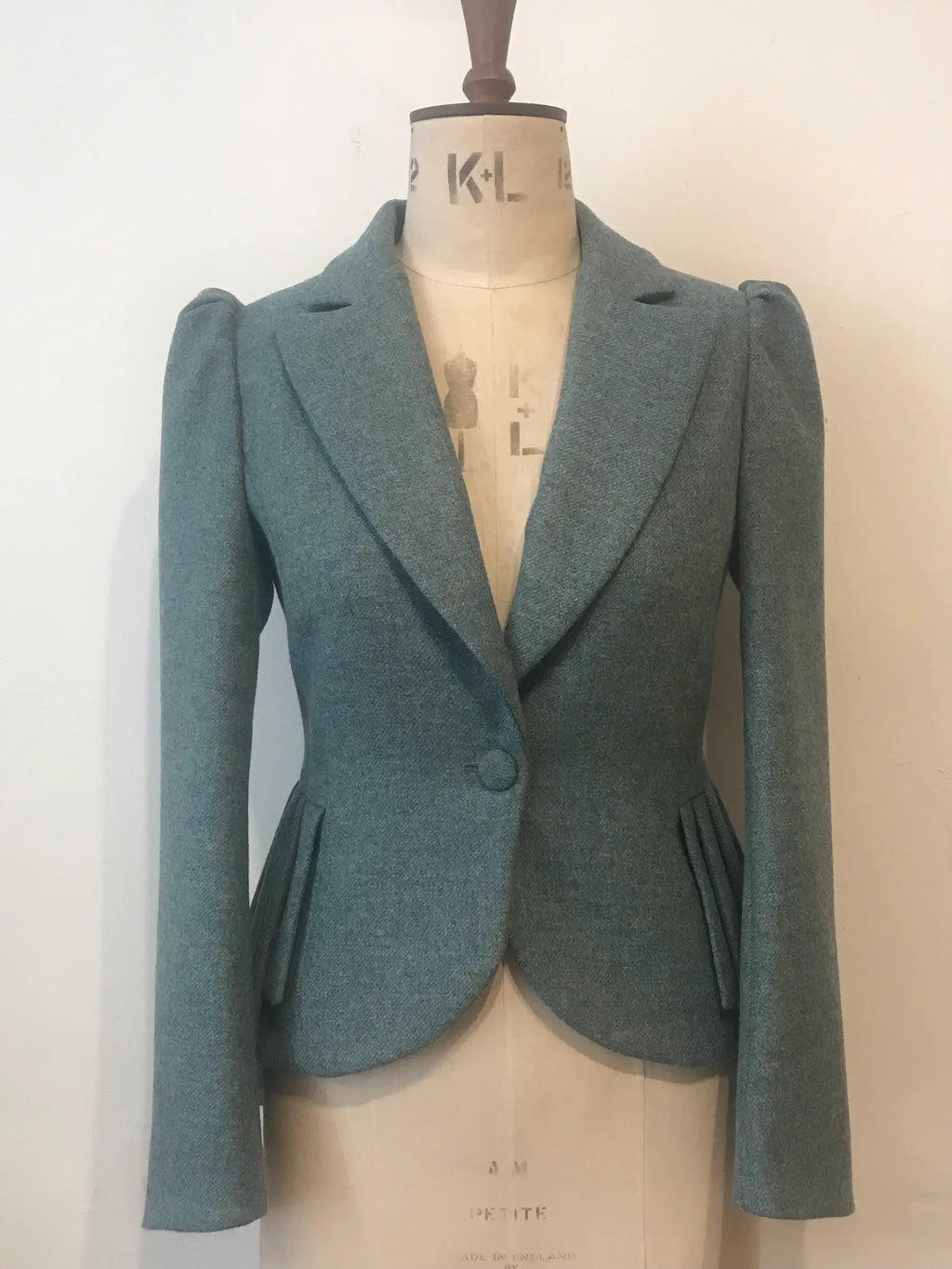 A Tweed Coachwoman Jacket displayed on a mannequin, in Nordic blue, with pleated side panels and a single-button closure.