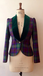 A velvet and tartan show jacket displayed on a mannequin, with the mannequin marked with 'KL' initials. The jacket has a classic silhouette with a green velvet collar and trim, and a multicolored tartan pattern.